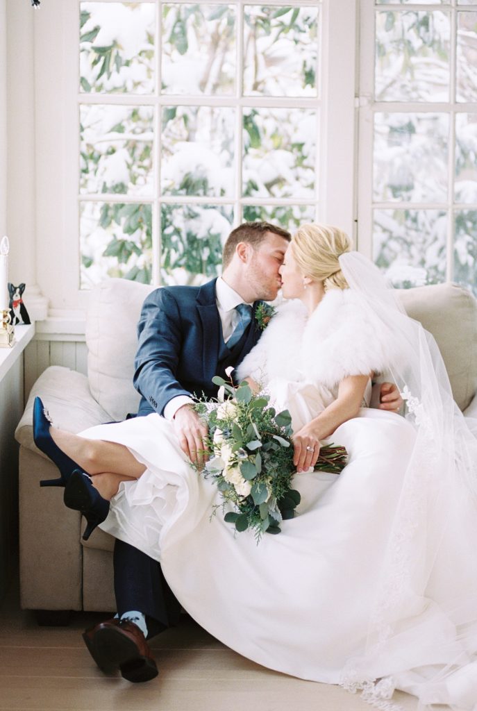 A newlywed couple kiss on the couch in their home